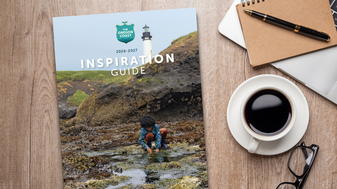 Oregon Coast Visitors Guide on a woodgrain table top to the side of a cup of coffee and a notbook.